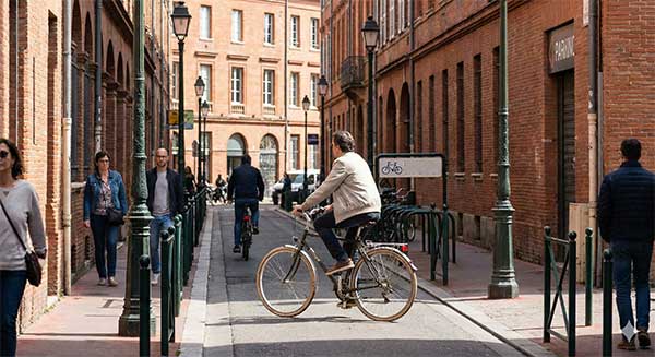 Cycliste-circulant-dans-une-rue-du-centre-historique-de-Toulouse,-se-dirigeant-de-la-place-Saint-Georges-vers-la-boutique-de-cigarette-électronique-Ismoke31,-avec-des-arceaux-vélo-disponibles-à-proximité